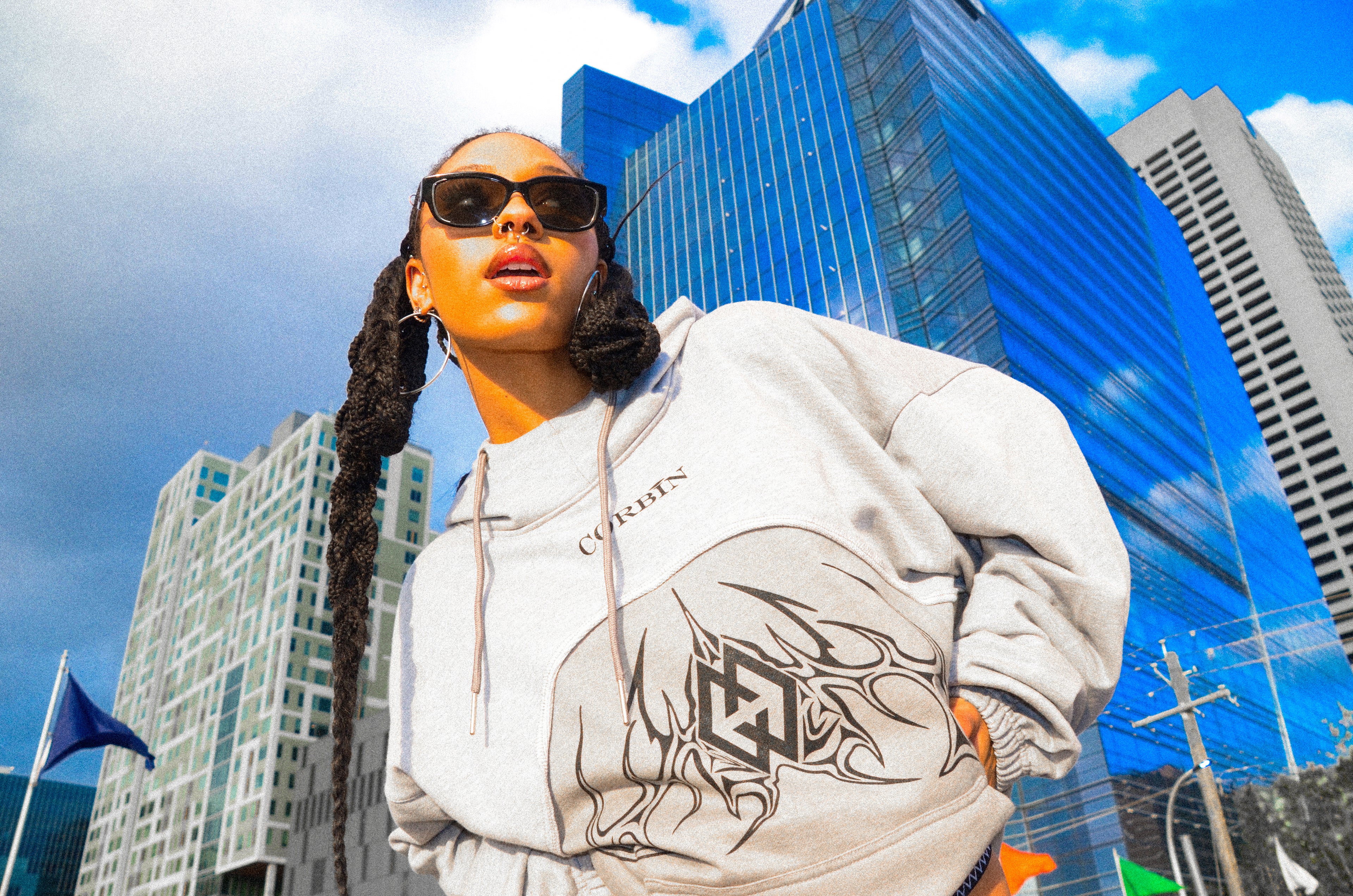 Stylish female model wearing a sleek gray Corbin hoodie, featuring a bold black logo centered on the chest for a modern, minimalist look.